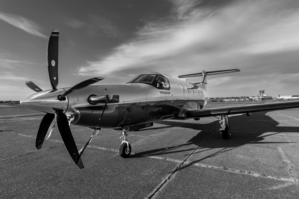 Black and white image of a private aircraft on an airfield under a clear sky.
